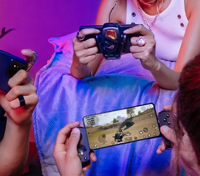 People gaming on ROG Phone with cooler attachment and handheld console showing action game on screen.