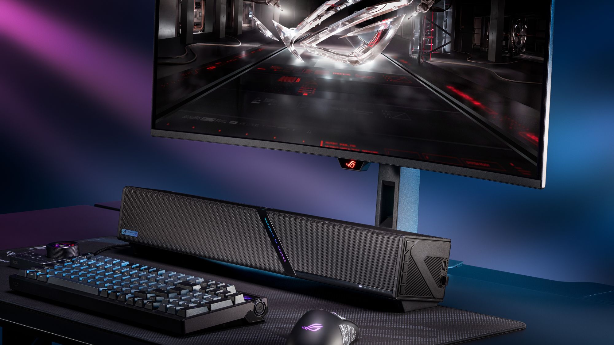 The ROG Gjallar gaming soundbar on a black desk surrounded by ROG gear and an ROG monitor.