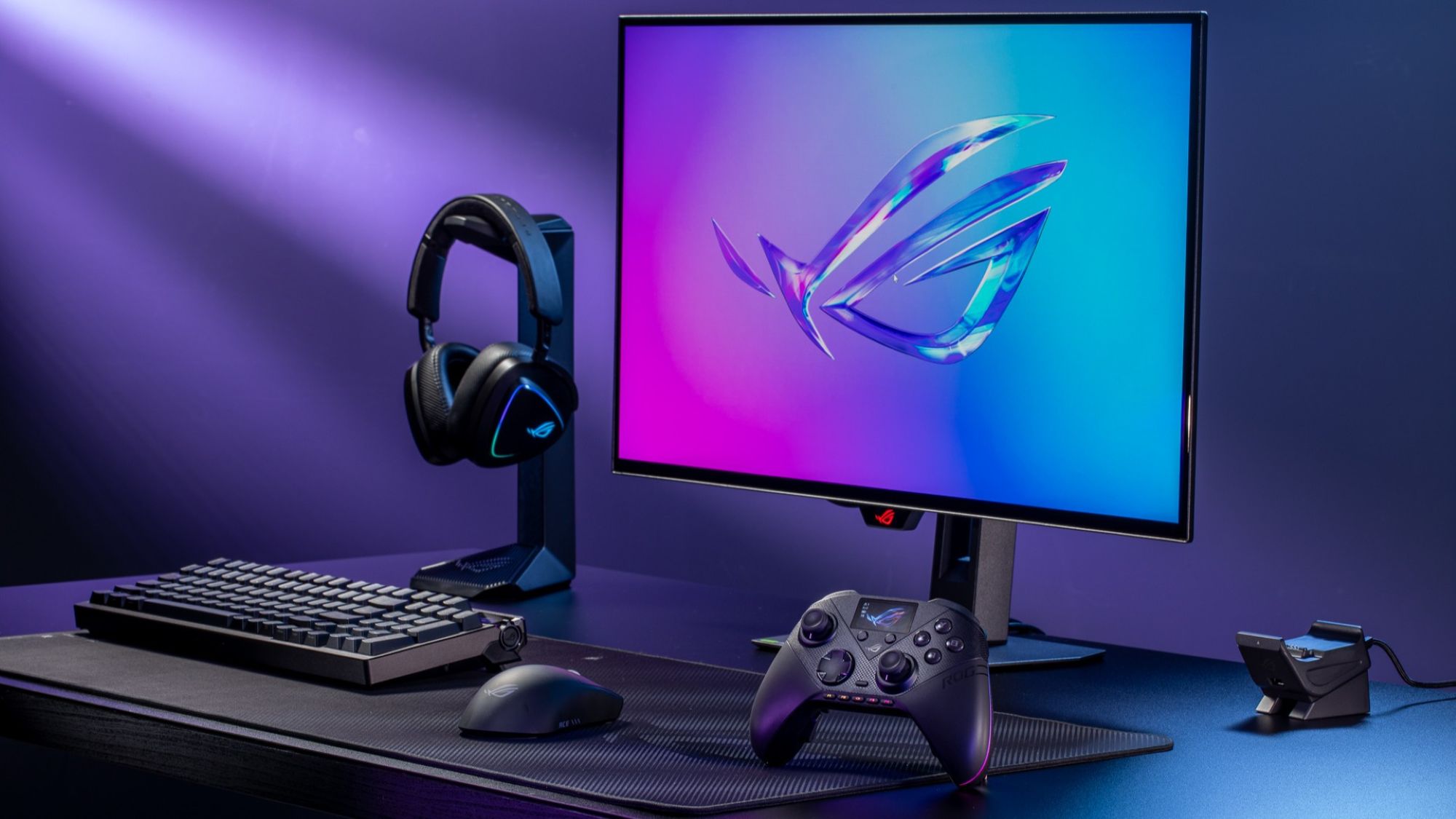 The ROG Raikiri II Pro PC Controller beside an ROG gaming setup featuring a keyboard and monitor on a black desk.