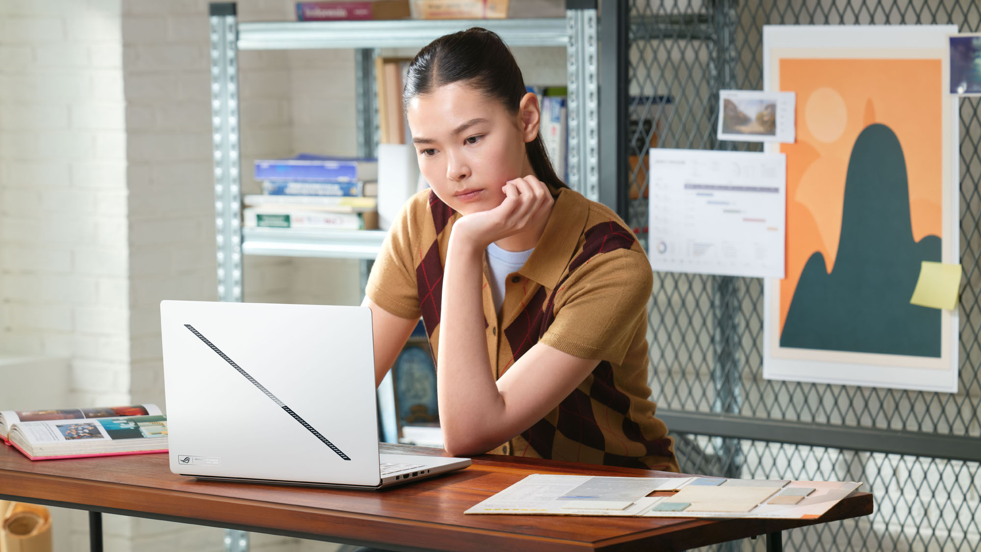 A woman using anROG Zephryus G14 at a desk with a textbook open