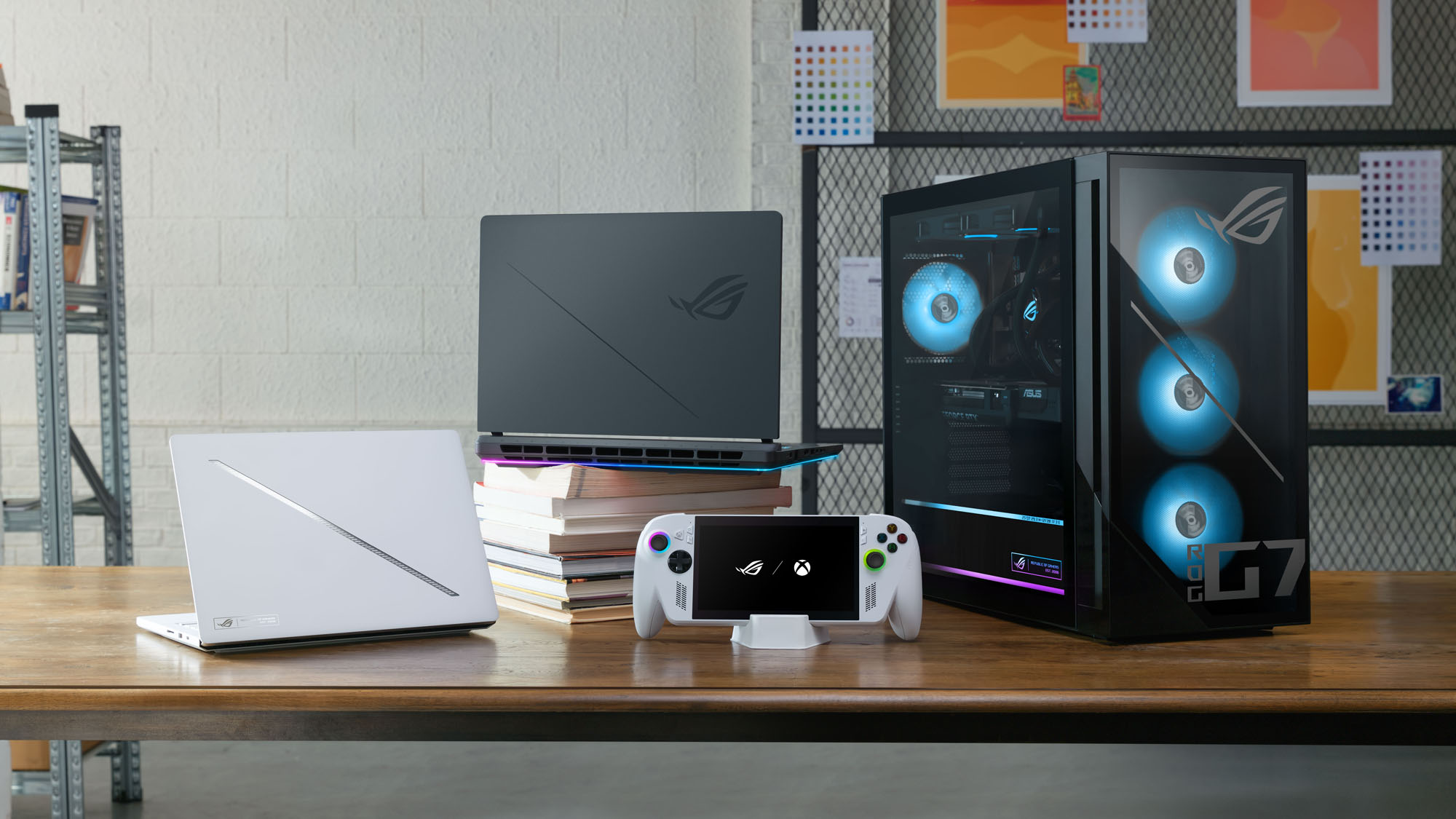 Two ROG laptops, an ROG desktop PC, and an ROG Ally on a table in a school library with books