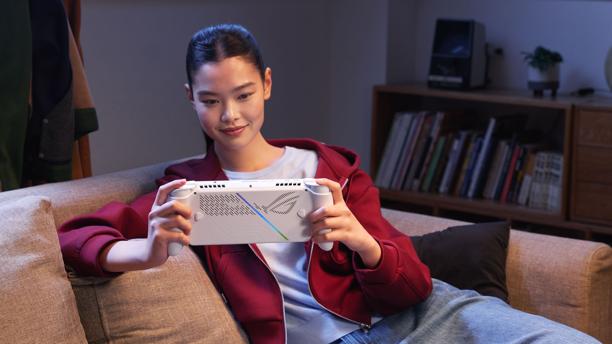 A woman sitting on a couch and smiling while playing the ROG XBOX Ally